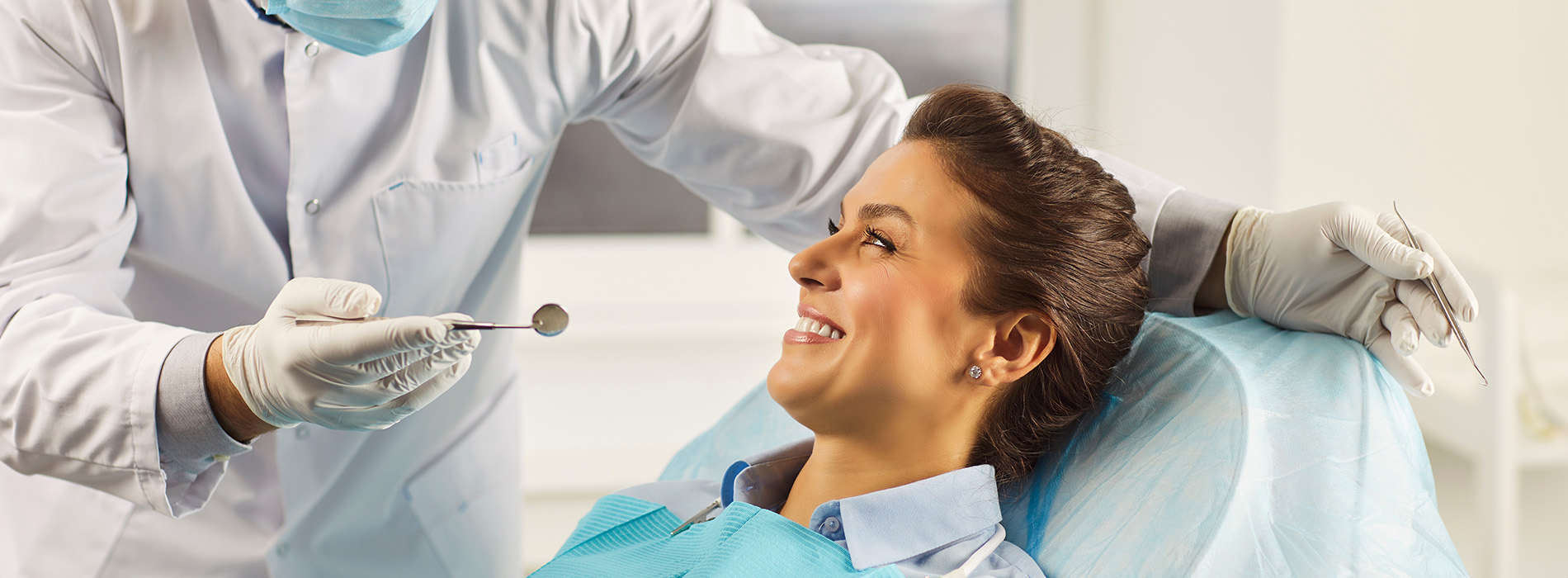 A person is seated in a dental chair, receiving care from a dental professional who stands behind them.